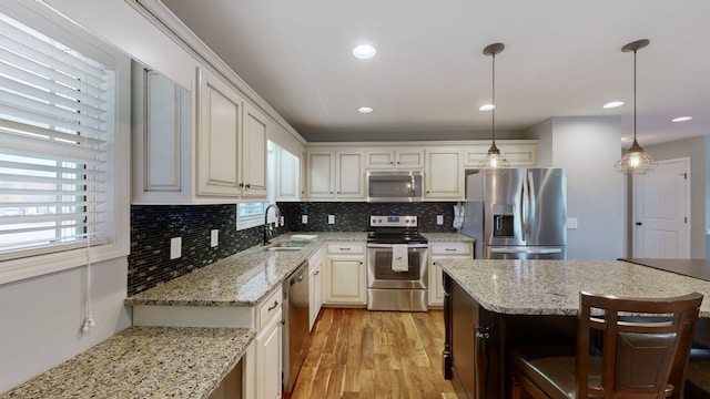 kitchen with appliances with stainless steel finishes, decorative light fixtures, sink, and light stone counters