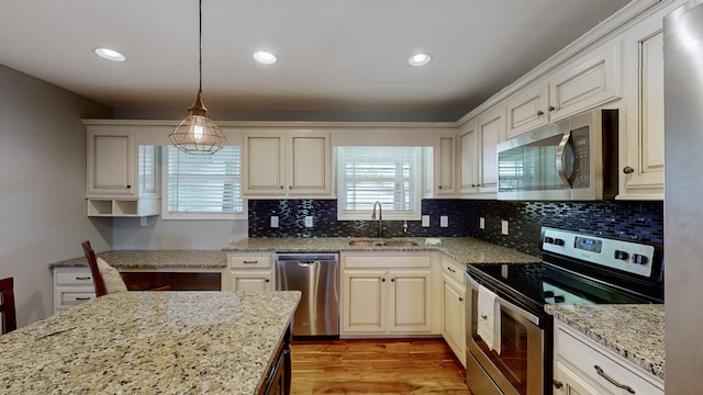 kitchen with stainless steel appliances, sink, light stone countertops, decorative light fixtures, and light wood-type flooring