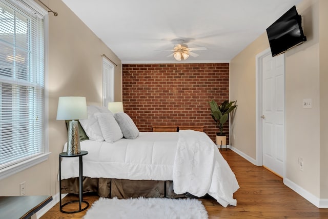 bedroom with brick wall, hardwood / wood-style flooring, and ceiling fan