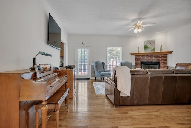 living room featuring light hardwood / wood-style flooring, ceiling fan, and a brick fireplace