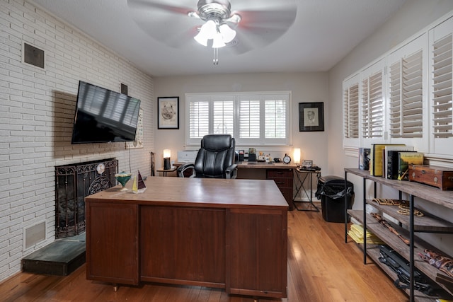 home office with light hardwood / wood-style floors, a brick fireplace, ceiling fan, and brick wall