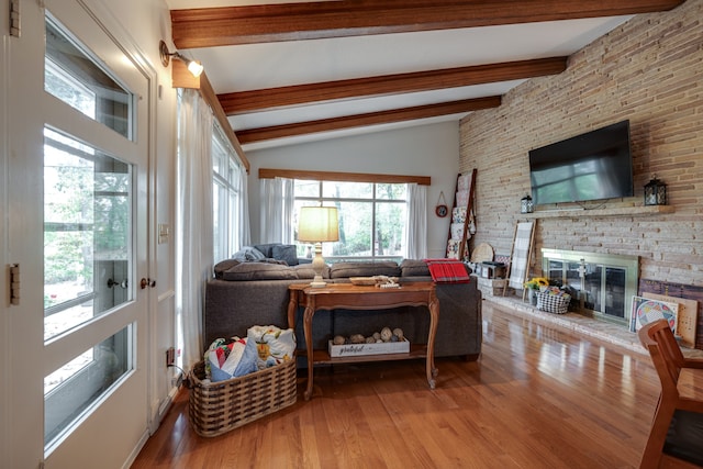 living room featuring vaulted ceiling with beams, light hardwood / wood-style floors, and a brick fireplace