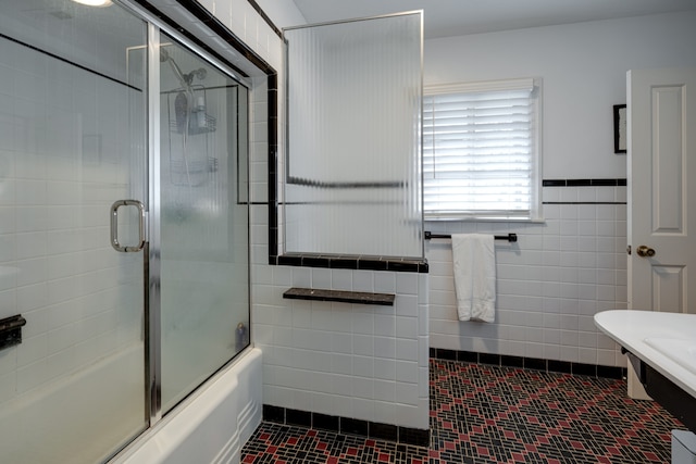 bathroom with tile walls and bath / shower combo with glass door