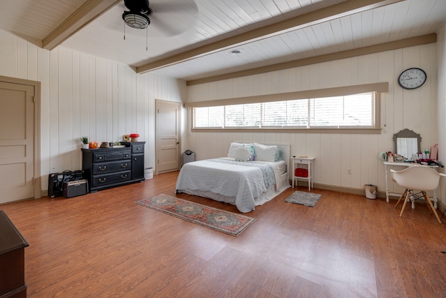 bedroom featuring ceiling fan, beam ceiling, wood-type flooring, and wooden walls