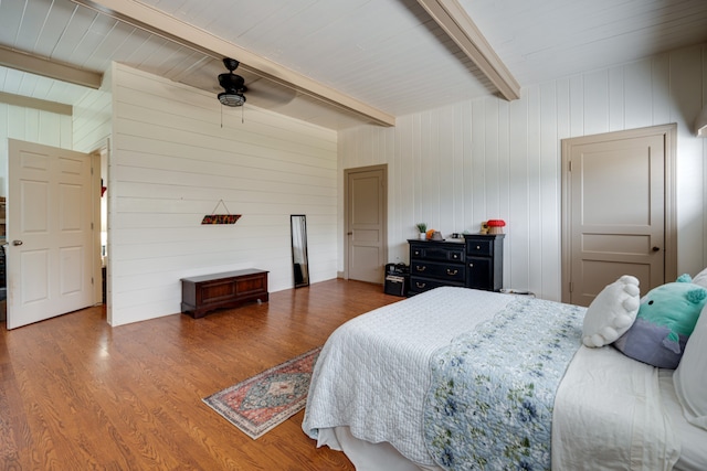 bedroom featuring beamed ceiling, hardwood / wood-style flooring, ceiling fan, and wooden walls