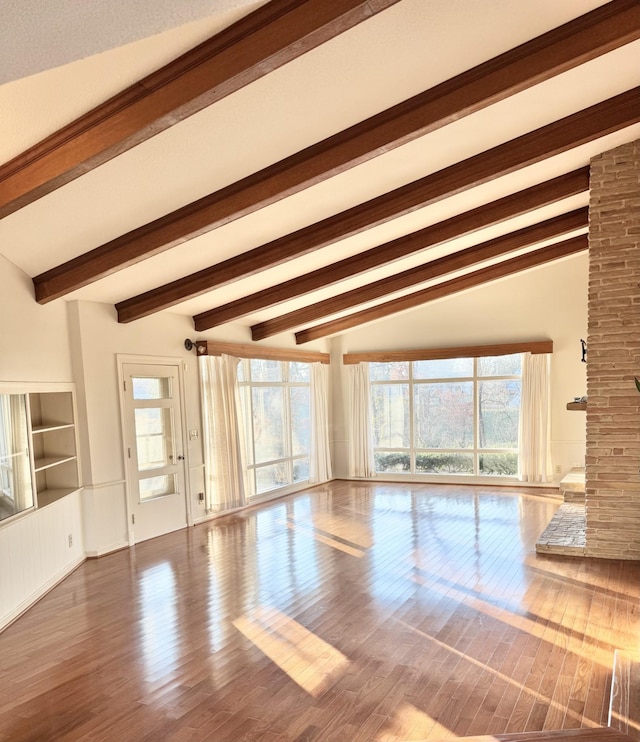 unfurnished living room featuring beamed ceiling, hardwood / wood-style floors, a fireplace, and a healthy amount of sunlight