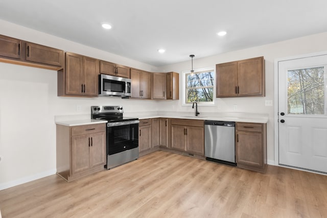 kitchen featuring appliances with stainless steel finishes, light hardwood / wood-style flooring, hanging light fixtures, and sink