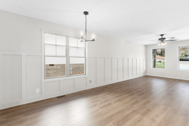 unfurnished dining area featuring ceiling fan with notable chandelier and light hardwood / wood-style flooring