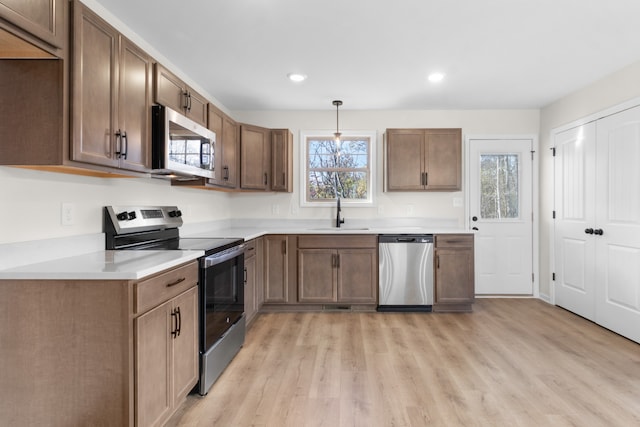 kitchen with light hardwood / wood-style floors, a wealth of natural light, hanging light fixtures, and appliances with stainless steel finishes