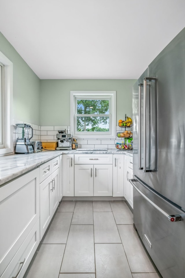 kitchen featuring white cabinets, light tile patterned flooring, light stone counters, and high end refrigerator