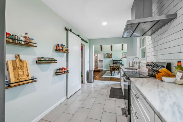 kitchen featuring sink, wall chimney exhaust hood, stainless steel range with electric cooktop, white cabinets, and a barn door