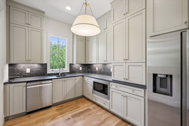 kitchen with decorative backsplash, sink, decorative light fixtures, light wood-type flooring, and appliances with stainless steel finishes