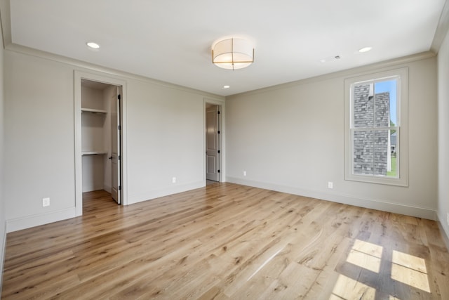 unfurnished bedroom featuring light hardwood / wood-style flooring, a walk in closet, ornamental molding, and a closet