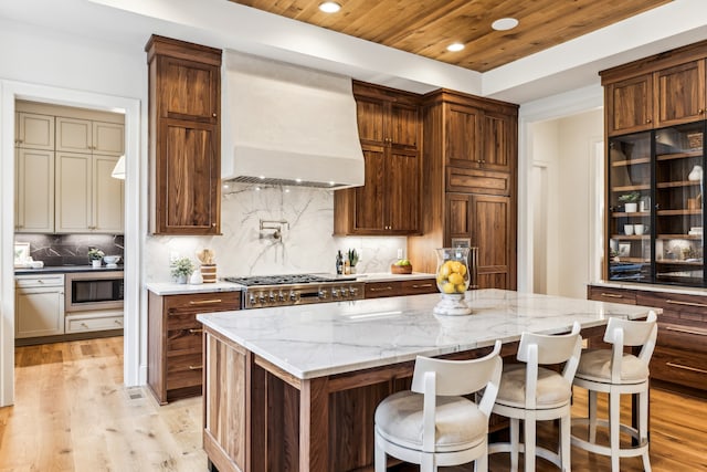 kitchen with a spacious island, premium range hood, light stone counters, and light hardwood / wood-style floors