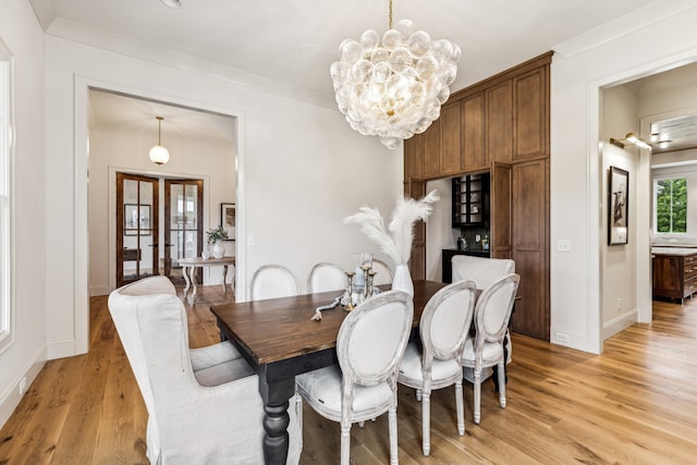 dining room featuring french doors, a notable chandelier, ornamental molding, and light wood-type flooring