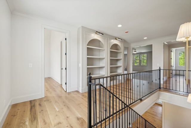 hall with a wealth of natural light, ornamental molding, and light hardwood / wood-style floors