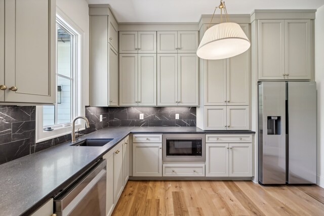 kitchen with appliances with stainless steel finishes, sink, backsplash, decorative light fixtures, and light hardwood / wood-style flooring