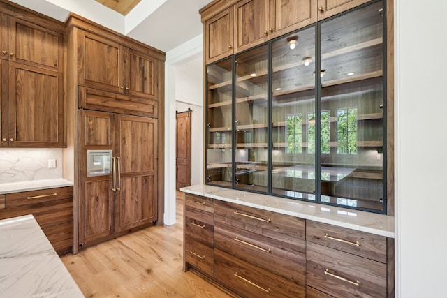 kitchen with light hardwood / wood-style flooring, decorative backsplash, a barn door, and light stone counters