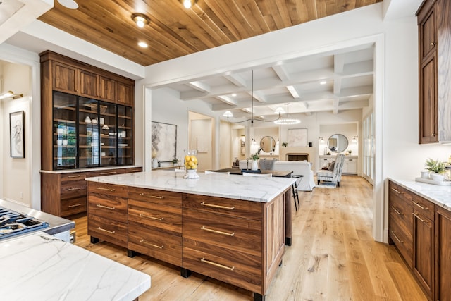 kitchen with beam ceiling, a kitchen island, light hardwood / wood-style flooring, and light stone counters