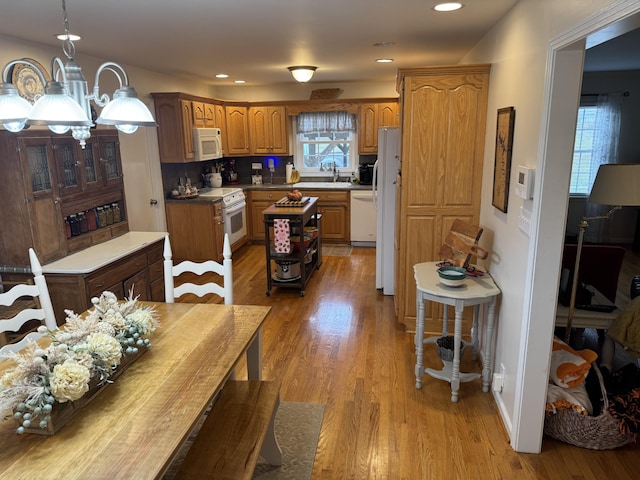 kitchen featuring sink, an inviting chandelier, pendant lighting, white appliances, and light hardwood / wood-style floors