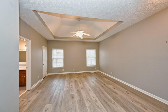 empty room with a raised ceiling, a textured ceiling, ceiling fan, and light hardwood / wood-style flooring