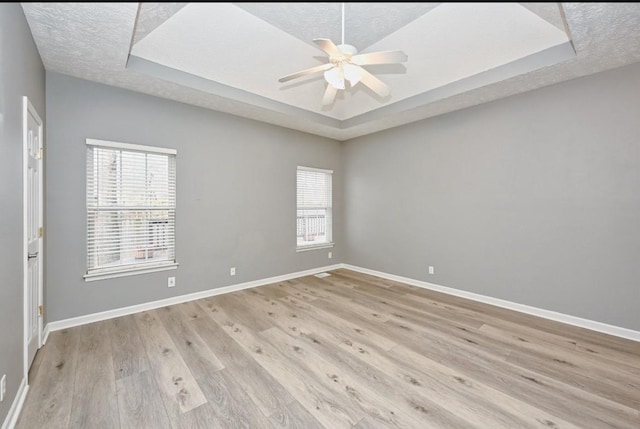 unfurnished room featuring a raised ceiling, plenty of natural light, a textured ceiling, and light hardwood / wood-style flooring