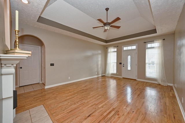 foyer featuring ceiling fan, light hardwood / wood-style flooring, a textured ceiling, and a tray ceiling