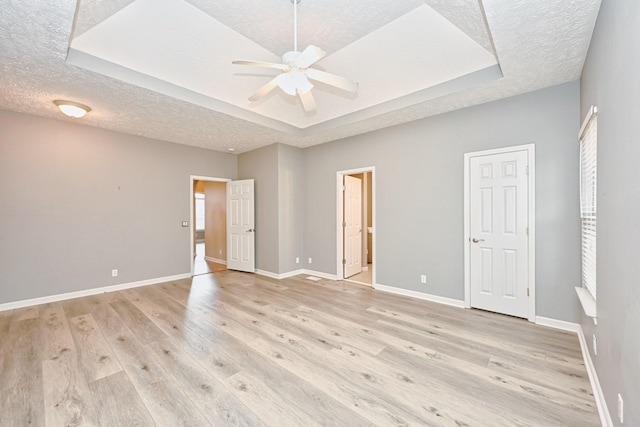 unfurnished bedroom with a tray ceiling, light hardwood / wood-style floors, and a textured ceiling