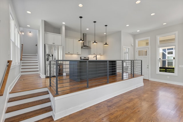 kitchen with wood-type flooring, wall chimney exhaust hood, decorative light fixtures, white cabinets, and stainless steel fridge with ice dispenser