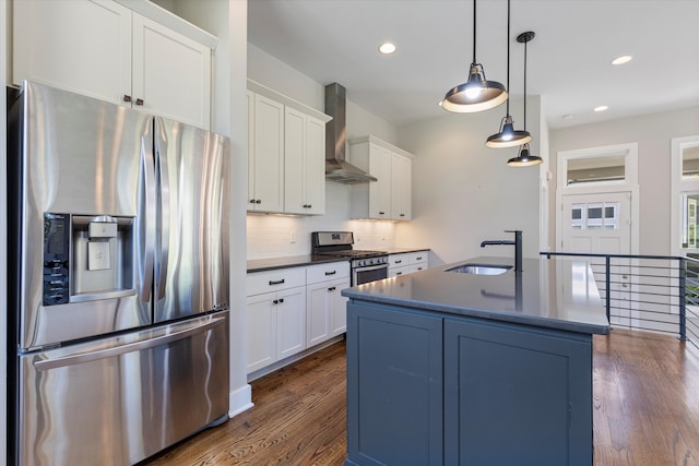 kitchen featuring wall chimney range hood, sink, hanging light fixtures, white cabinetry, and stainless steel appliances