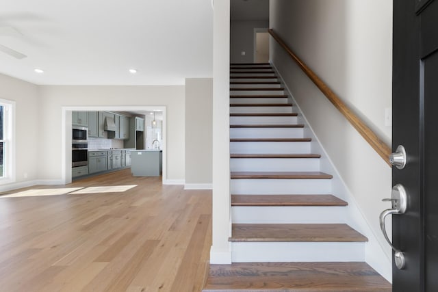 stairway with wood-type flooring, sink, and ceiling fan