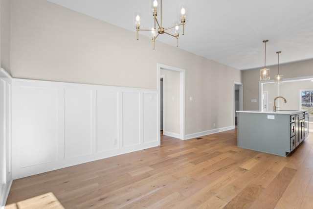 kitchen featuring sink, a center island with sink, light wood-type flooring, and decorative light fixtures