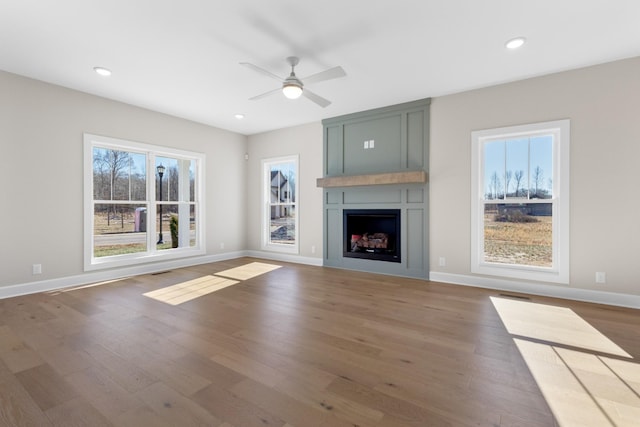 unfurnished living room with ceiling fan, wood-type flooring, a fireplace, and a wealth of natural light