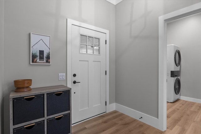 foyer entrance with stacked washer / drying machine and light hardwood / wood-style flooring