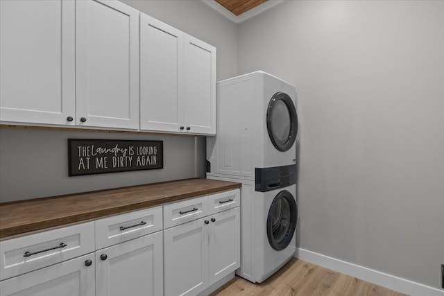 clothes washing area featuring cabinets, light hardwood / wood-style flooring, and stacked washer and dryer