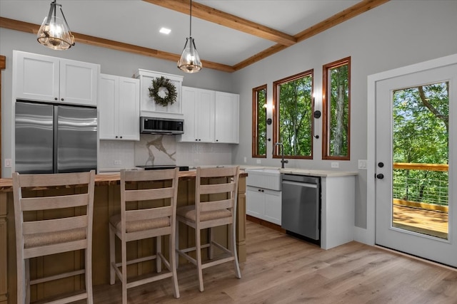 kitchen with white cabinets, light hardwood / wood-style flooring, stainless steel appliances, and decorative light fixtures