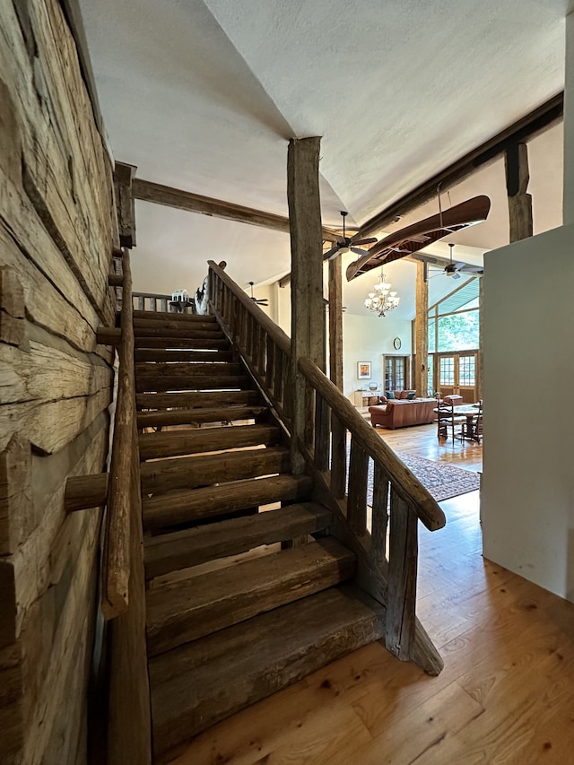 stairs featuring lofted ceiling, a textured ceiling, wood-type flooring, and ceiling fan with notable chandelier