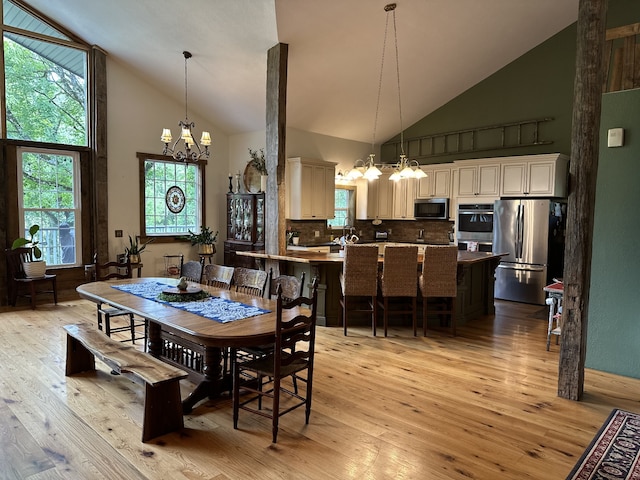 dining area with light hardwood / wood-style flooring, high vaulted ceiling, and an inviting chandelier