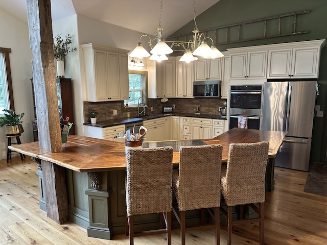 kitchen with a chandelier, vaulted ceiling, stainless steel appliances, and light wood-type flooring