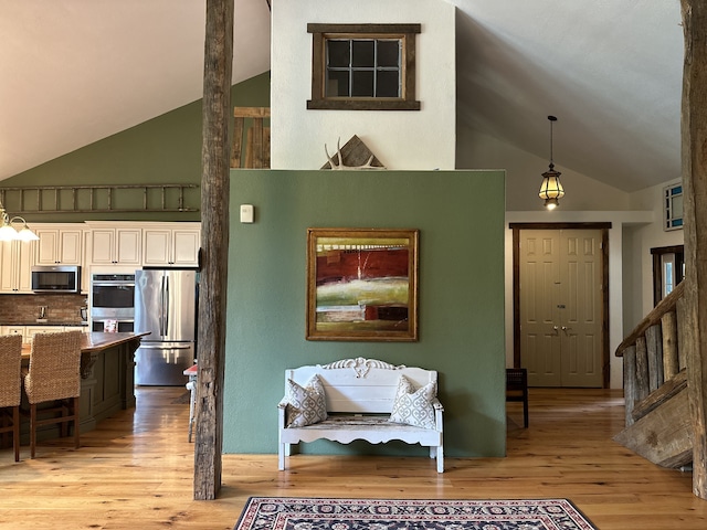 interior space featuring light wood-type flooring, hanging light fixtures, stainless steel appliances, white cabinets, and high vaulted ceiling