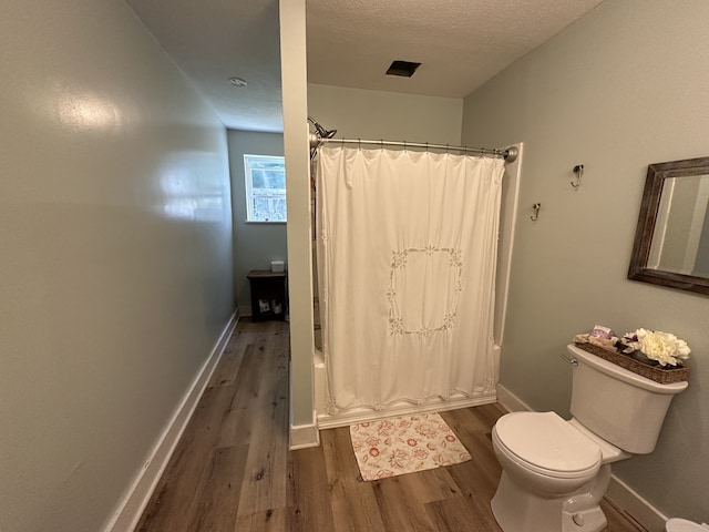 bathroom featuring shower / tub combo, a textured ceiling, hardwood / wood-style flooring, and toilet