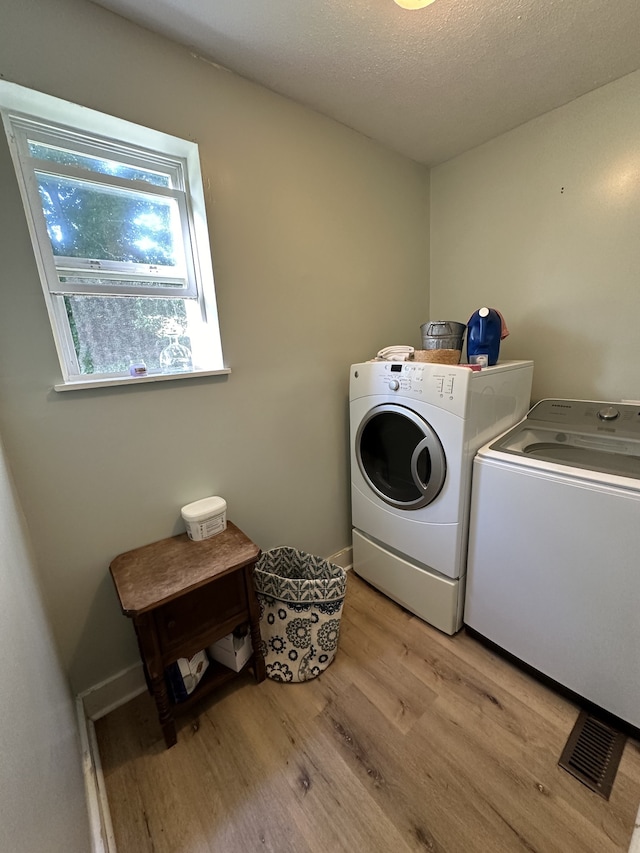 clothes washing area with light hardwood / wood-style flooring, a textured ceiling, and washing machine and dryer