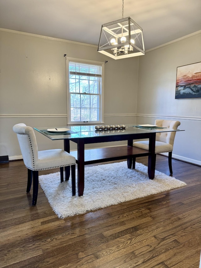 dining area featuring dark wood-type flooring, ornamental molding, and a notable chandelier