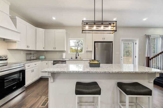 kitchen with appliances with stainless steel finishes, a kitchen island, white cabinetry, custom exhaust hood, and dark wood-type flooring