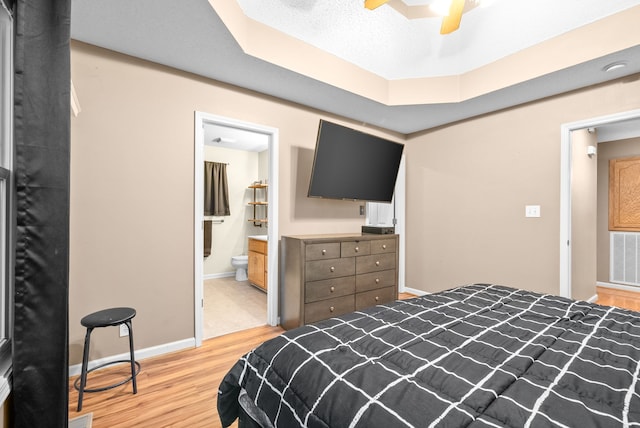 bedroom with ceiling fan, ensuite bathroom, a textured ceiling, and light wood-type flooring