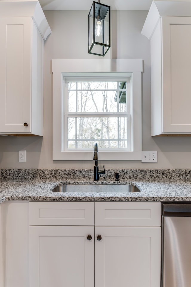 interior space featuring light stone counters, white cabinetry, hanging light fixtures, and sink