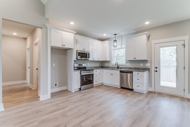 kitchen with pendant lighting, white cabinets, light wood-type flooring, and appliances with stainless steel finishes