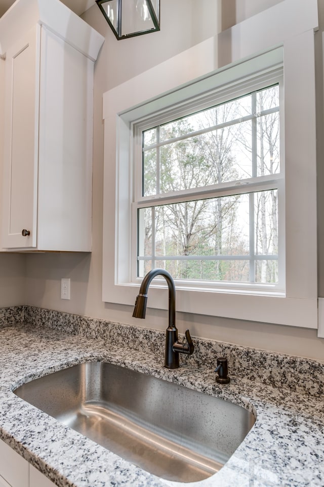 interior details featuring light stone countertops, sink, and white cabinets