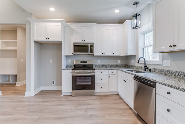 kitchen featuring appliances with stainless steel finishes, light wood-type flooring, light stone counters, sink, and white cabinetry