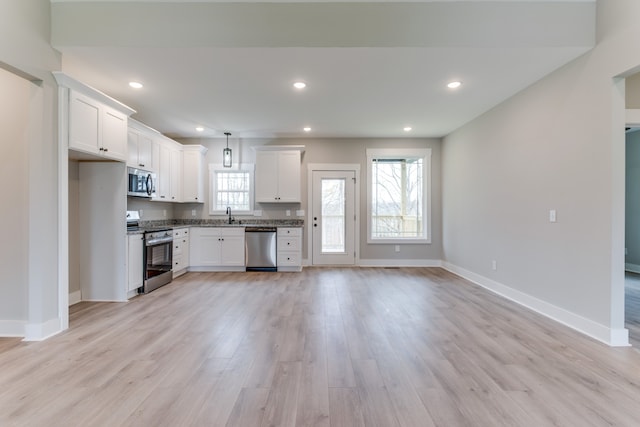 kitchen with light wood-type flooring, stainless steel appliances, sink, white cabinetry, and hanging light fixtures